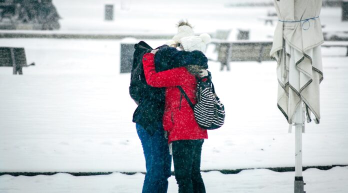 Photo by Christian Lue person in red and black jacket and black pants carrying white dog on snow covered ground