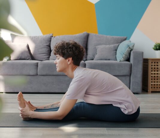만성피로, 바쁜 일상 속 에너지 되찾는 ‘소소한 실천’이 해법 Woman stretching on yoga mat in living room.