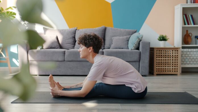 Woman stretching on yoga mat in living room.
